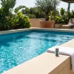 Une piscine à l'eau bleue cristalline avec un testeur de qualité et une serviette sur le bord, entourée de végétation luxuriante.